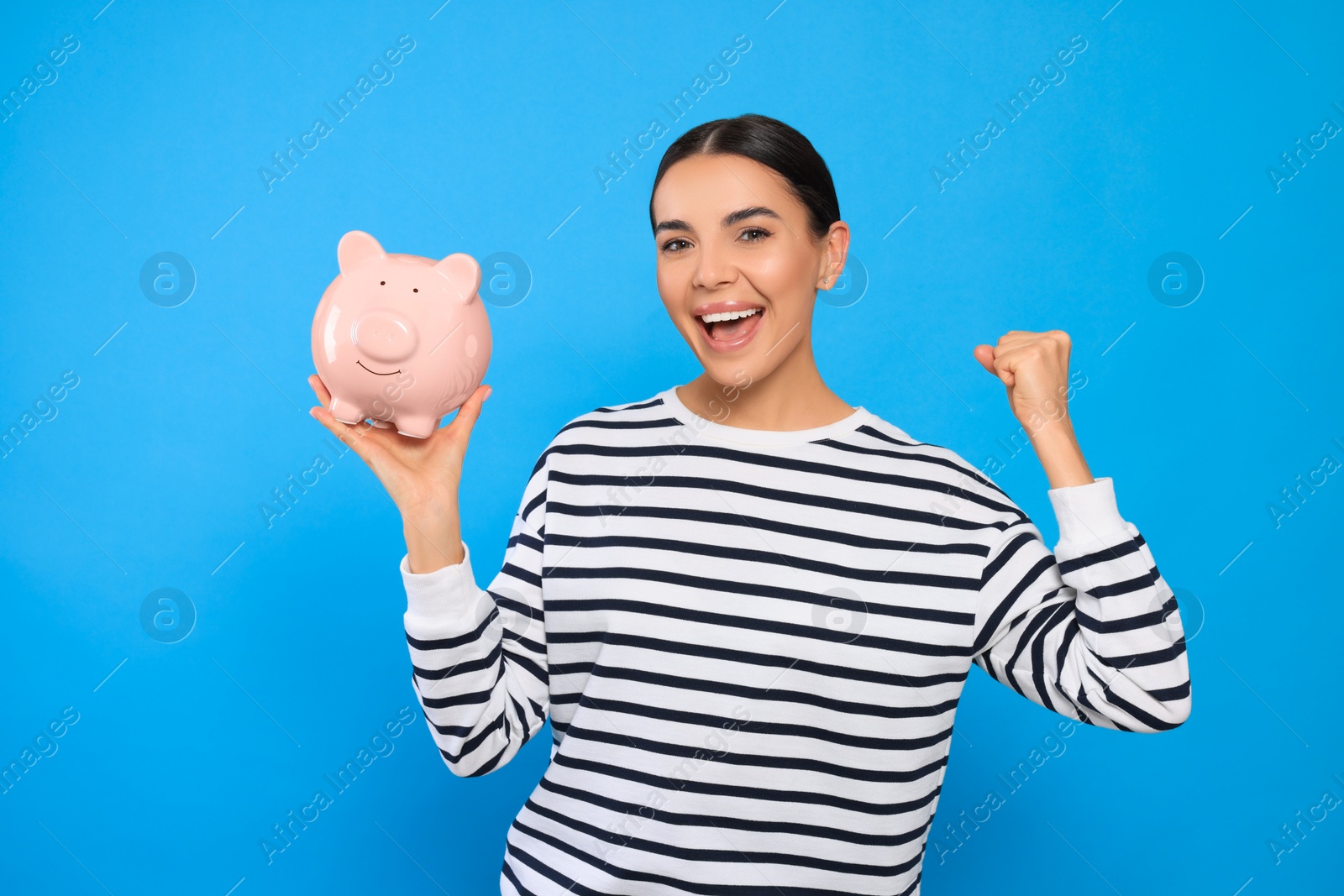 Photo of Emotional young woman with piggy bank on light blue background