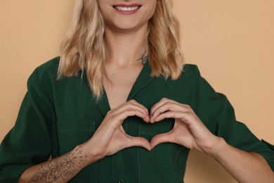 Photo of Happy volunteer making heart with her hands on beige background, closeup