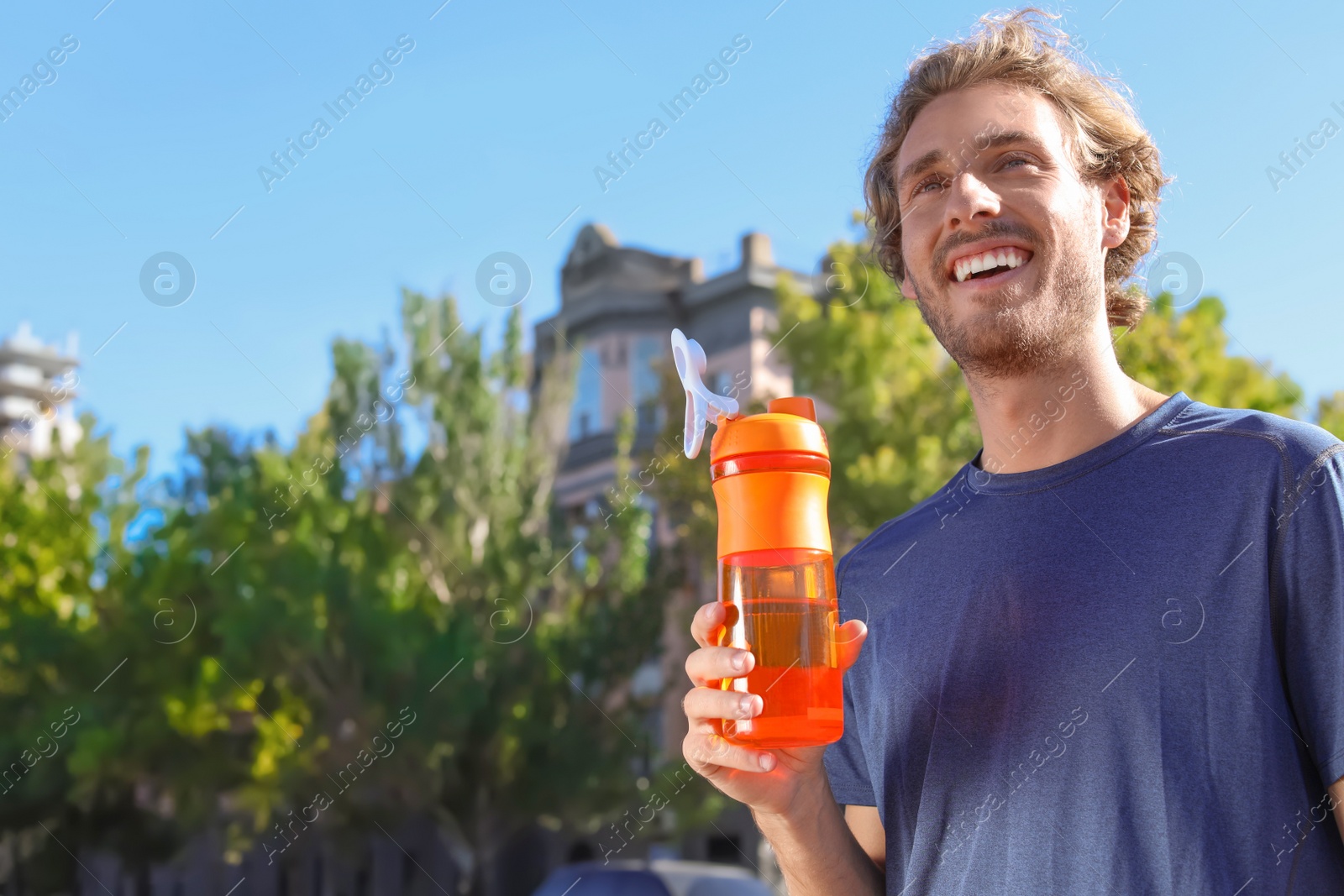 Photo of Young man holding bottle with clean water outdoors. Space for text