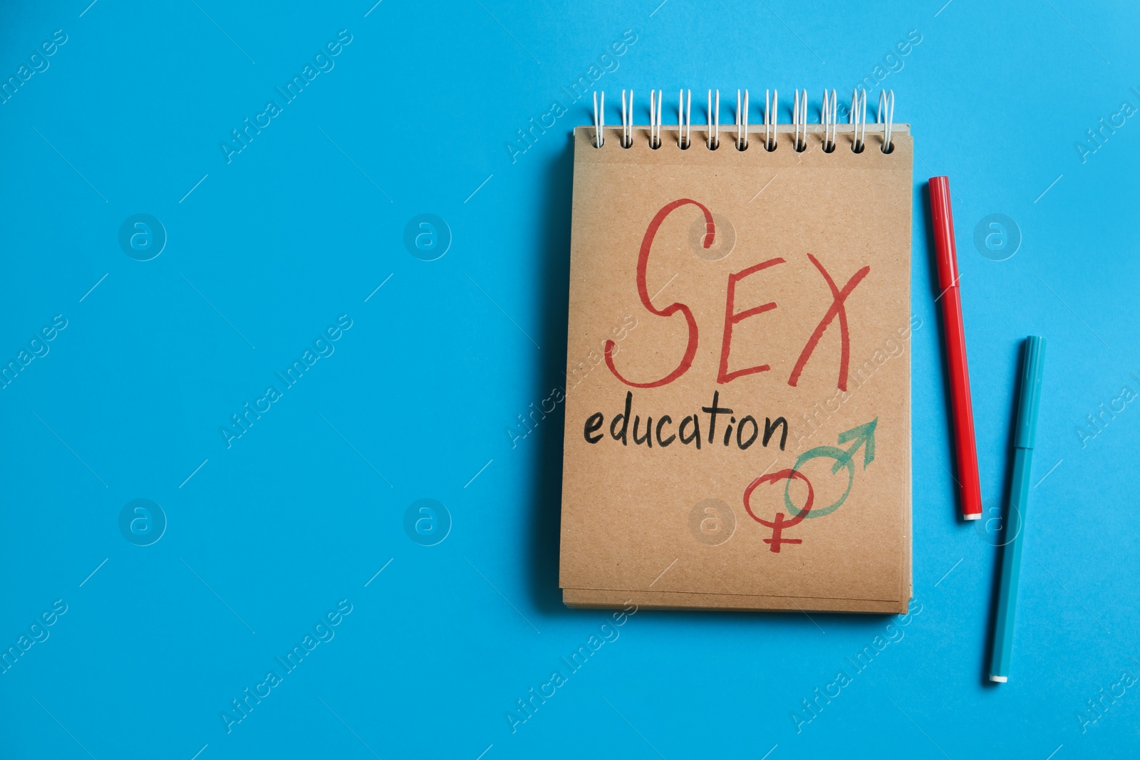 Photo of Notebook with phrase "SEX EDUCATION" and gender symbols on blue background, flat lay. Space for text
