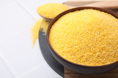 Photo of Raw cornmeal in bowl on white tiled table, closeup. Space for text