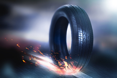 Image of Car tire with flame rolling on road against blurred background