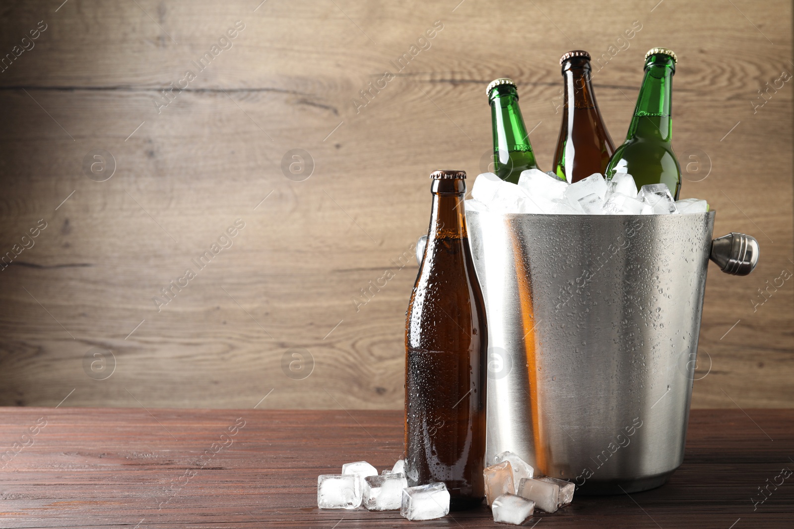 Photo of Metal bucket with beer and ice cubes on wooden table. Space for text