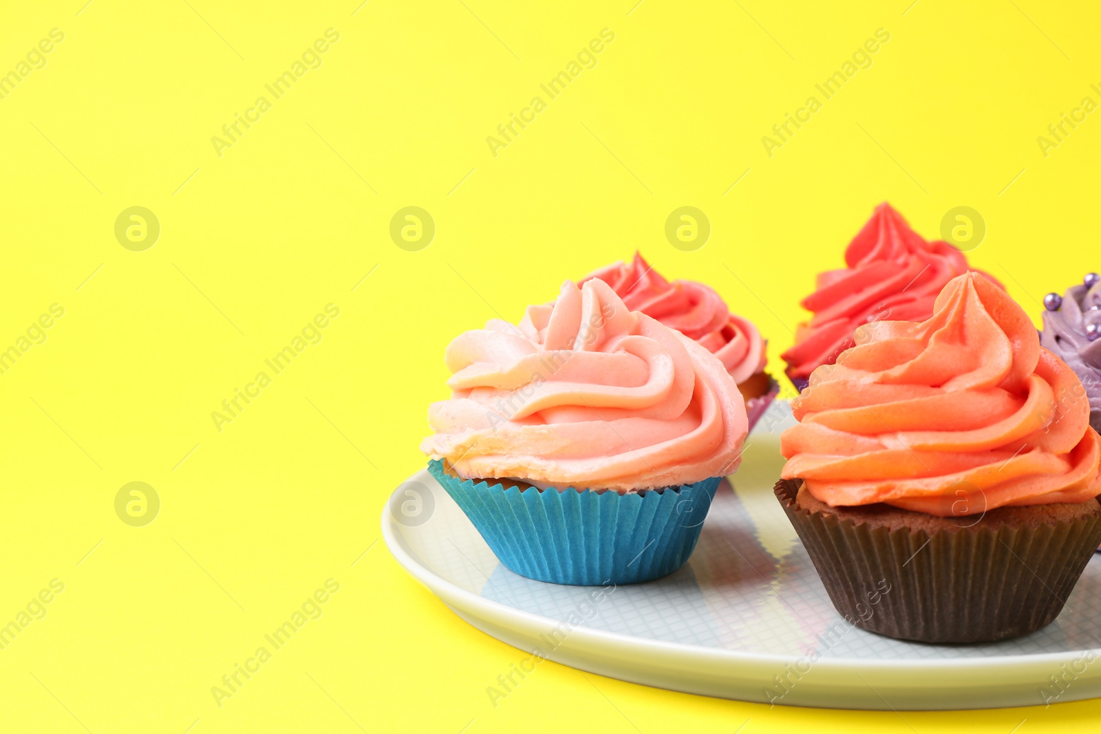 Photo of Delicious cupcakes with bright cream on yellow background. Space for text