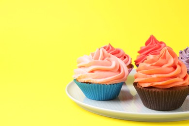 Photo of Delicious cupcakes with bright cream on yellow background. Space for text