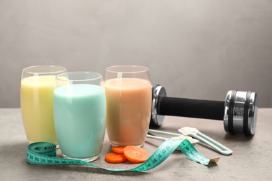 Photo of Tasty shakes, dumbbell, measuring tape and pieces of carrot on gray table, space for text. Weight loss