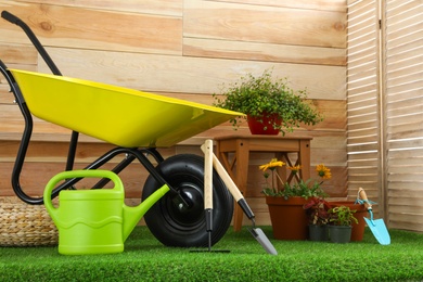 Photo of Wheelbarrow with gardening tools and flowers near wooden wall