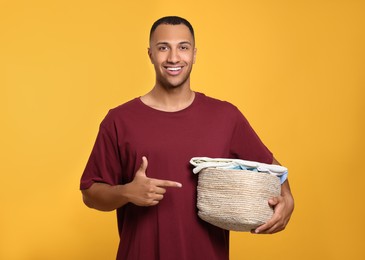 Photo of Happy man with basket full of laundry on orange background