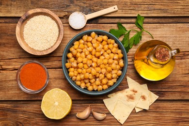 Photo of Delicious chickpeas and different ingredients on wooden table, flat lay. Cooking hummus