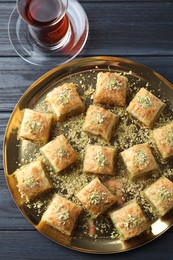 Photo of Delicious fresh baklava with chopped nuts and tea on black wooden table, top view. Eastern sweets