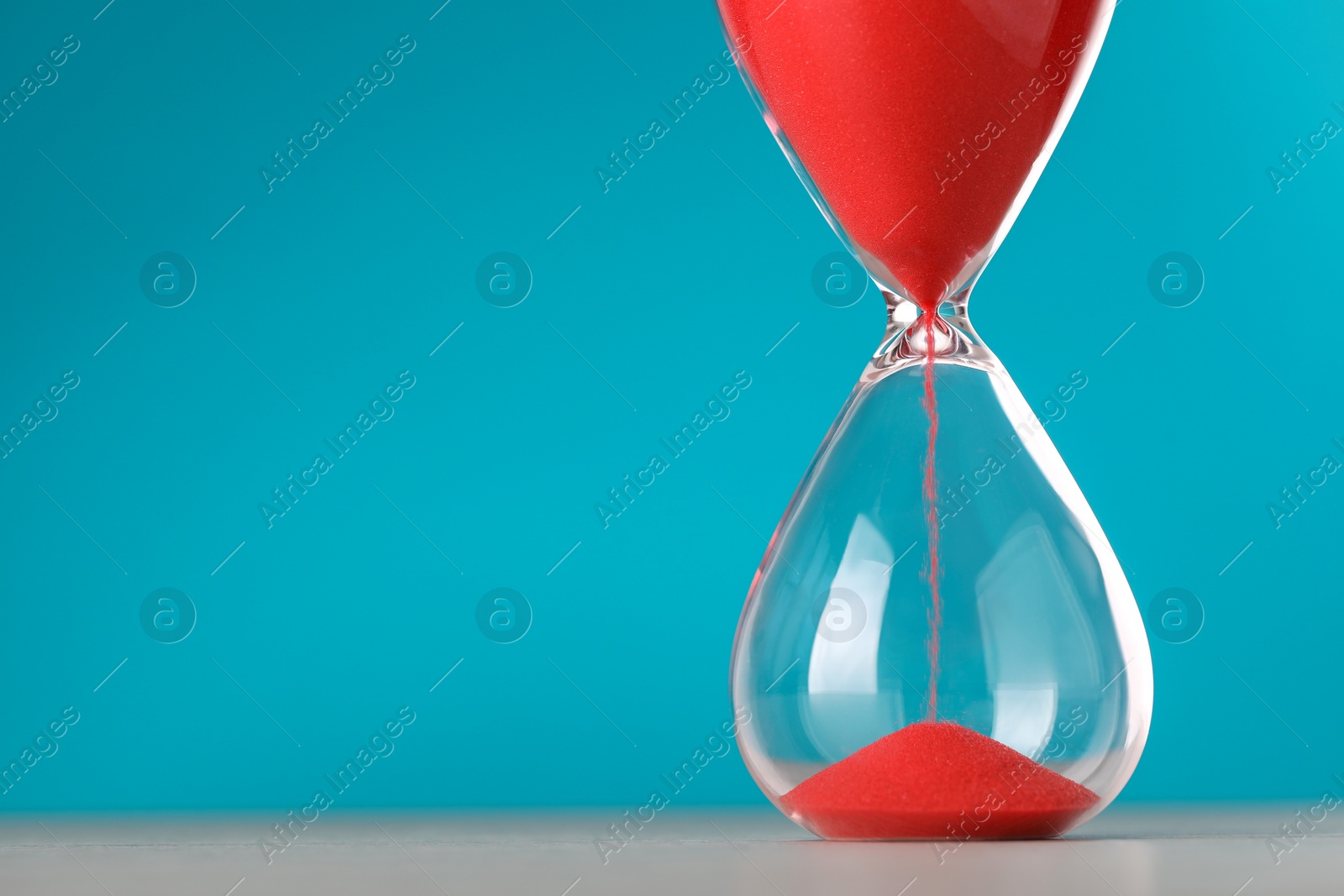 Photo of Hourglass with flowing red sand on table against light blue background, space for text