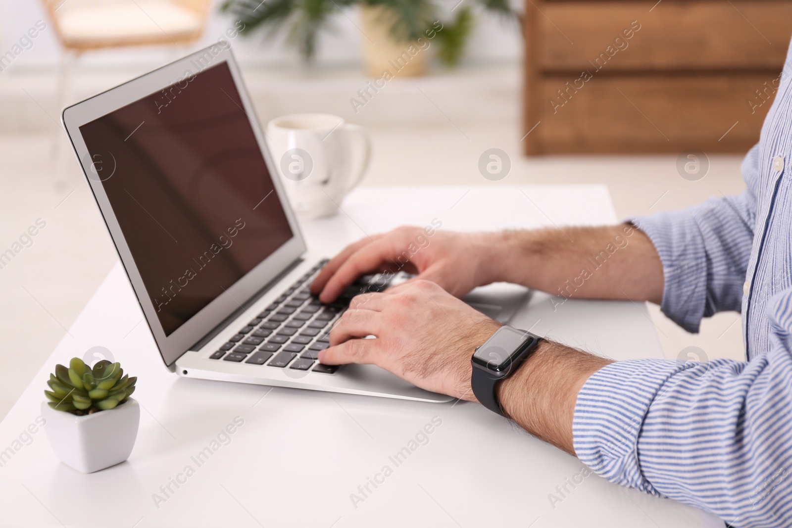 Photo of Young man with smart watch working on laptop at table in office, closeup