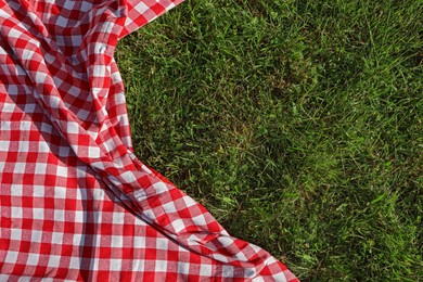 Photo of Checkered picnic tablecloth on fresh green grass, top view. Space for text