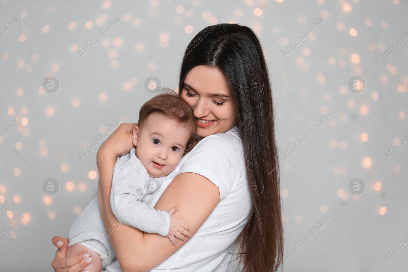 Photo of Portrait of young mother and her adorable baby against defocused lights