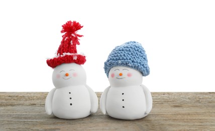 Photo of Cute decorative snowmen in hats on wooden table against white background