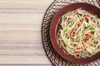 Plate of noodles with broth and vegetables on table, top view. Space for text