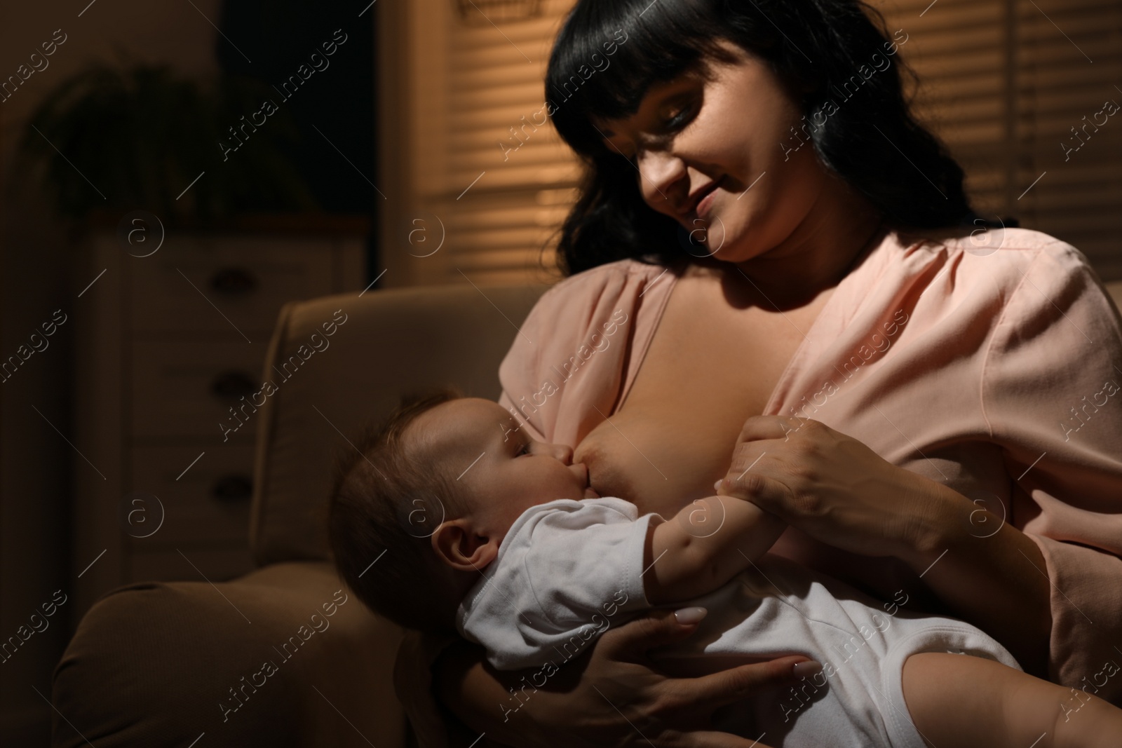 Photo of Woman breastfeeding her little baby on sofa in evening