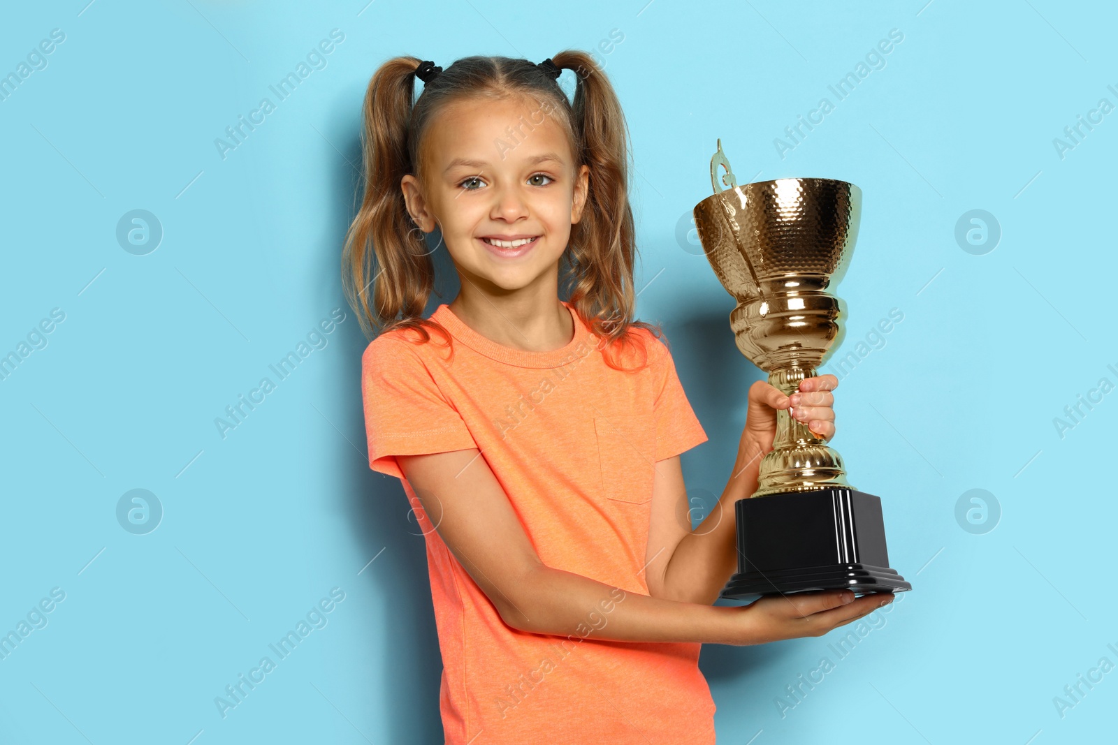 Photo of Happy girl with golden winning cup on blue background