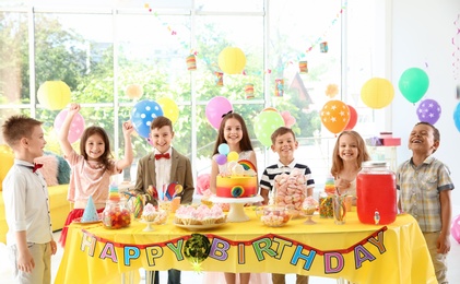 Cute children near table with treats at birthday party indoors