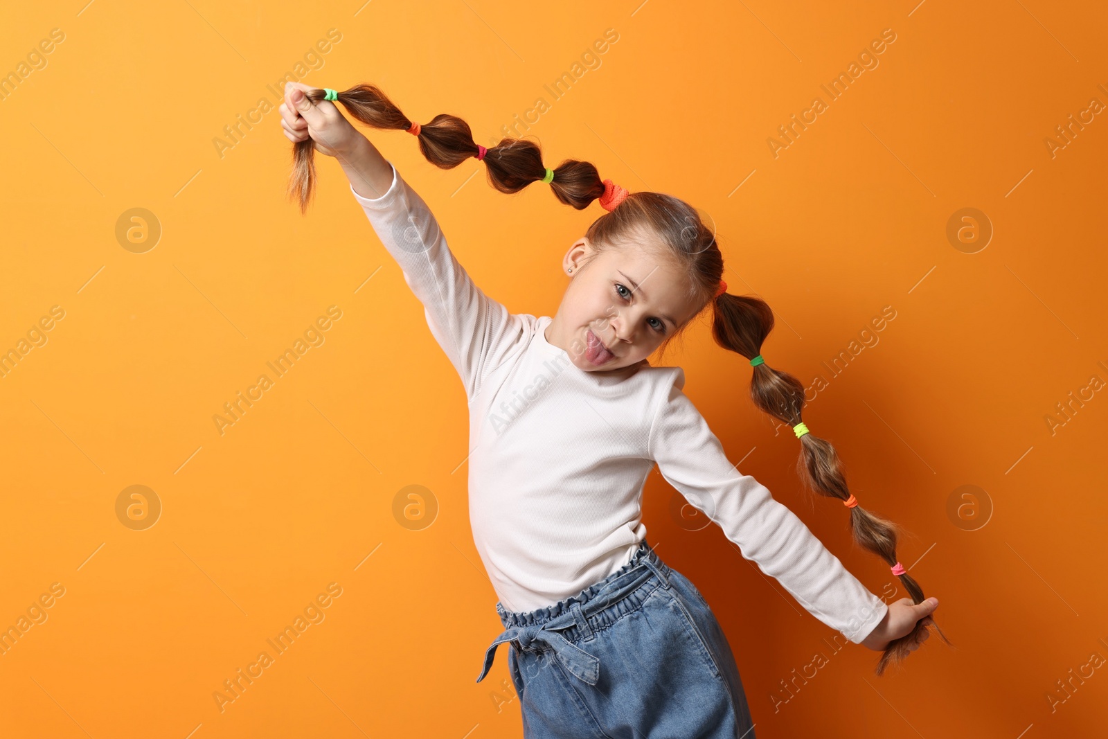 Photo of Cute little girl with beautiful hairstyle having fun on orange background