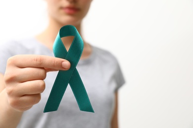 Photo of Woman holding teal awareness ribbon against light background, closeup