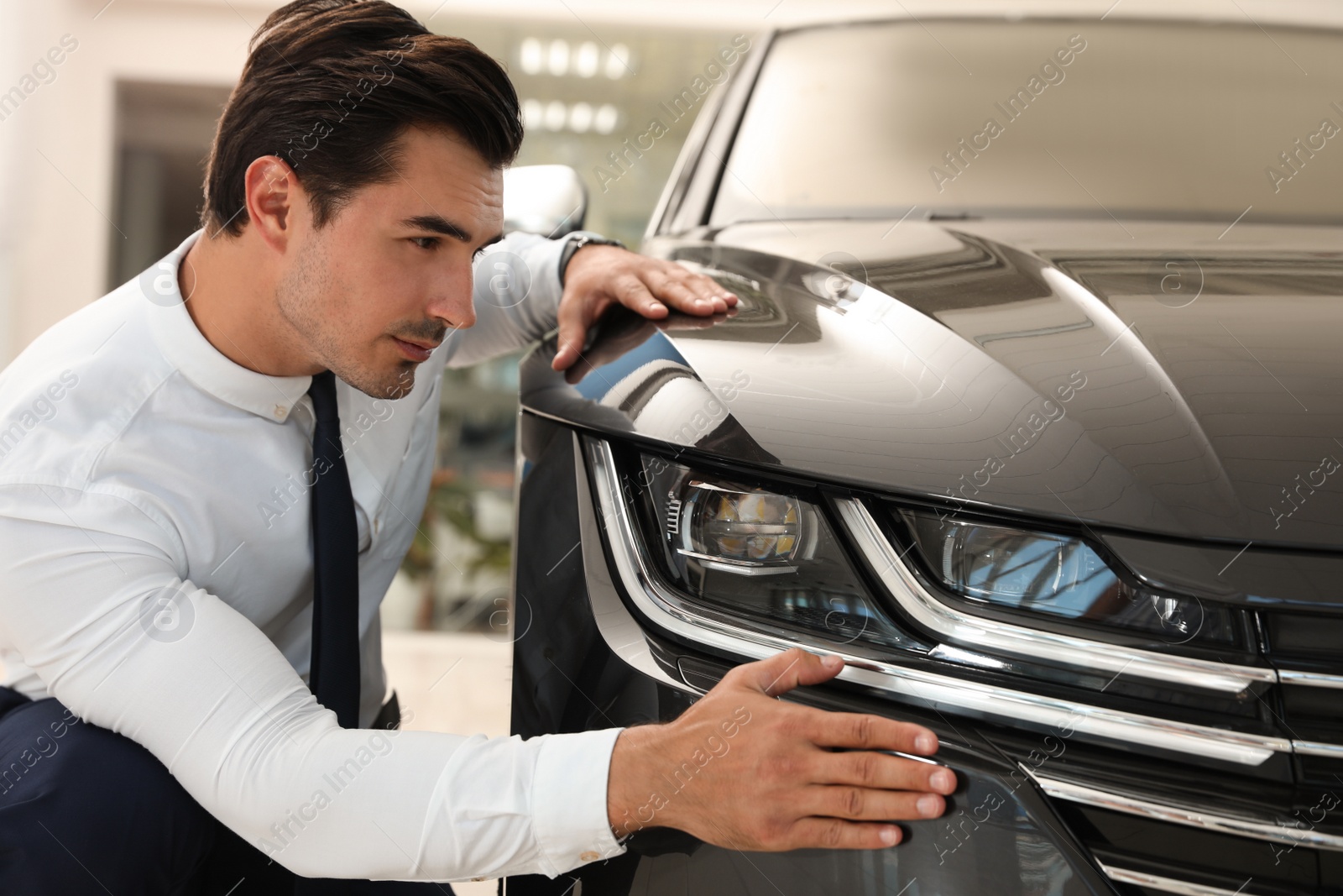 Photo of Young man checking new car in modern dealership