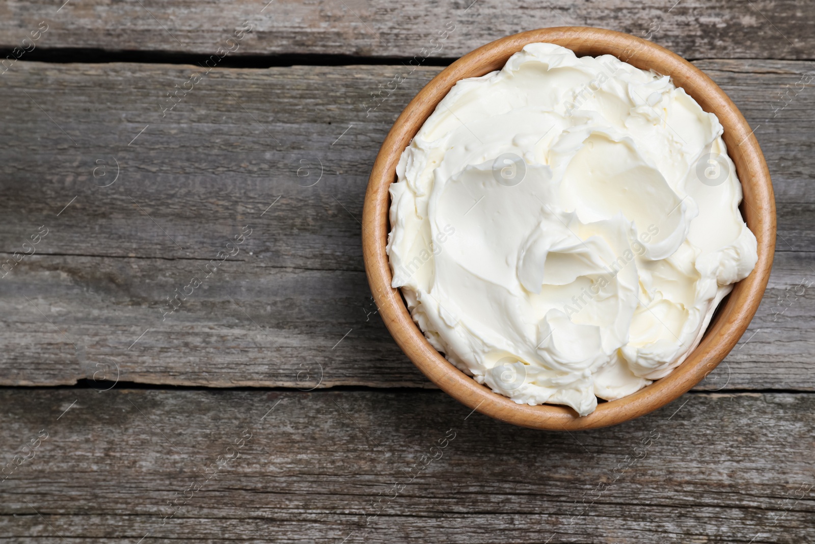 Photo of Bowl of tasty cream cheese on wooden table, top view. Space for text
