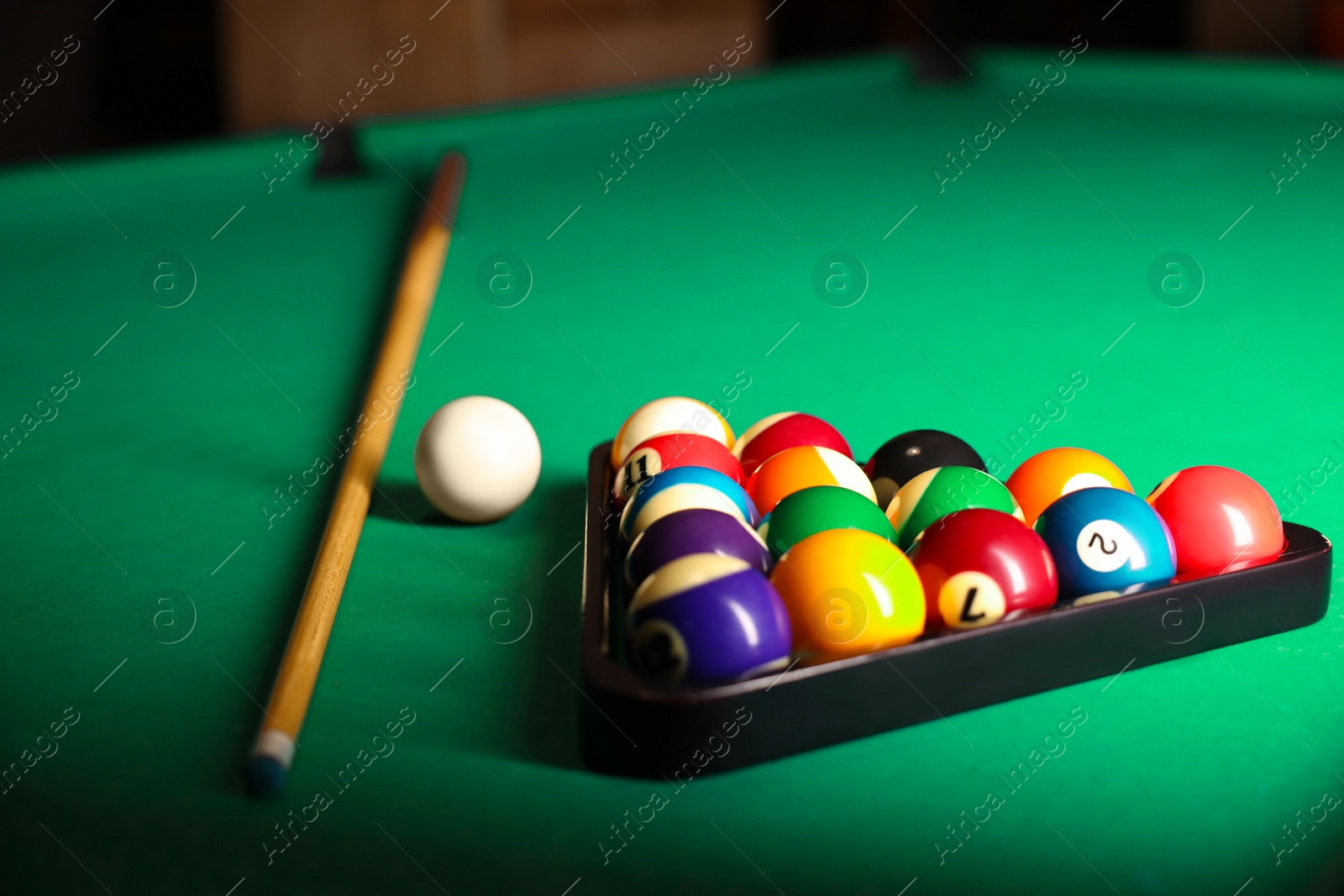 Photo of Plastic triangle rack with billiard balls and cue on green table, closeup