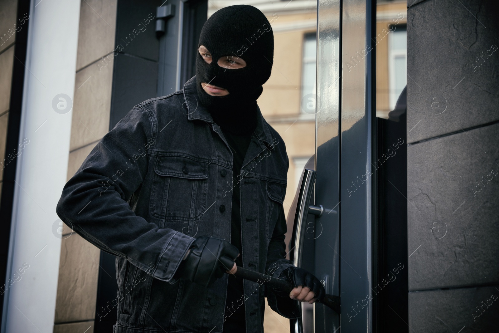 Photo of Man in mask forcing door with crow bar. Dangerous criminal