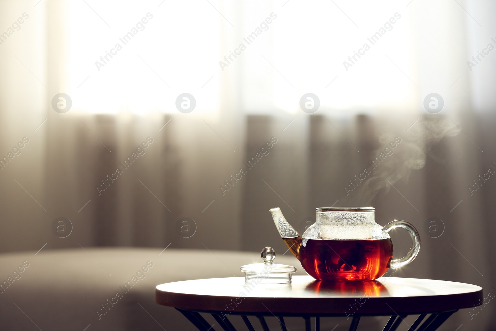 Photo of Teapot of fresh hot tea on table against blurred background. Space for text