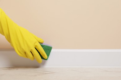 Photo of Woman in protective glove cleaning plinth with sponge indoors, closeup. Space for text