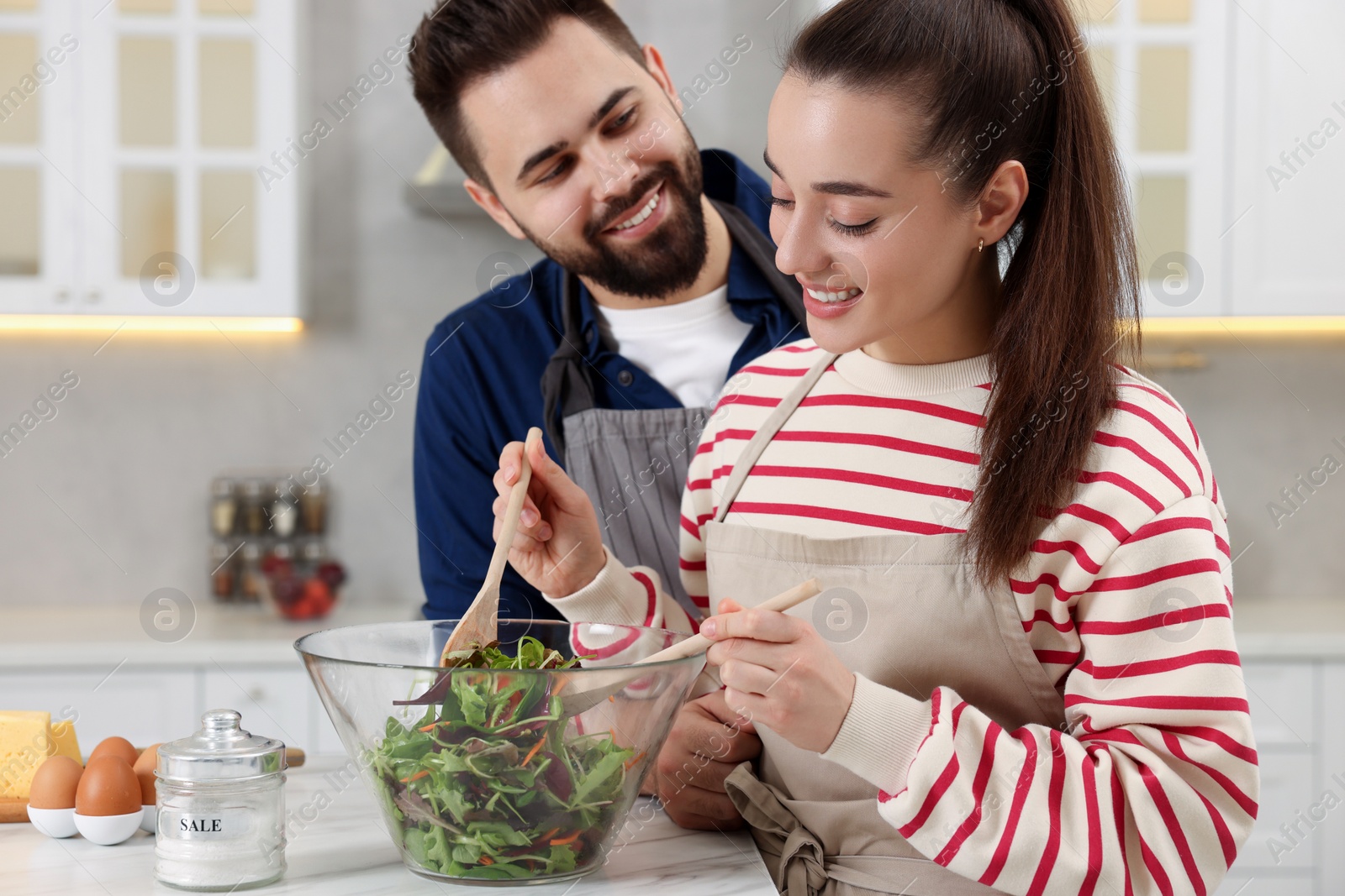 Photo of Happy affectionate couple cooking together at white table in kitchen