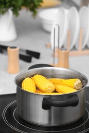 Photo of Stewpot with water and corn cobs on stove in kitchen