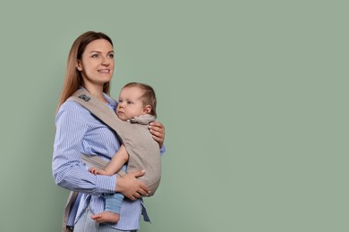 Photo of Mother holding her child in sling (baby carrier) on olive background. Space for text