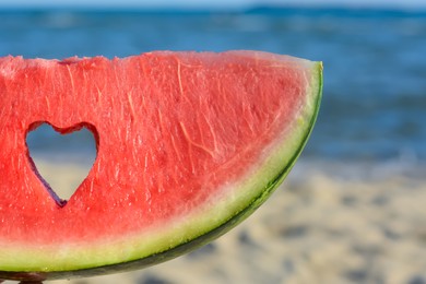 Photo of Child holding slice of watermelon with heart shaped hole near sea, closeup