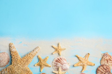 Beautiful sea stars, shells and sand on light blue background, flat lay. Space for text