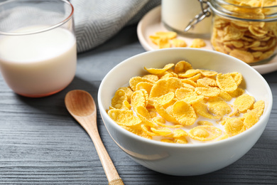 Photo of Tasty crispy corn flakes with milk on grey wooden table