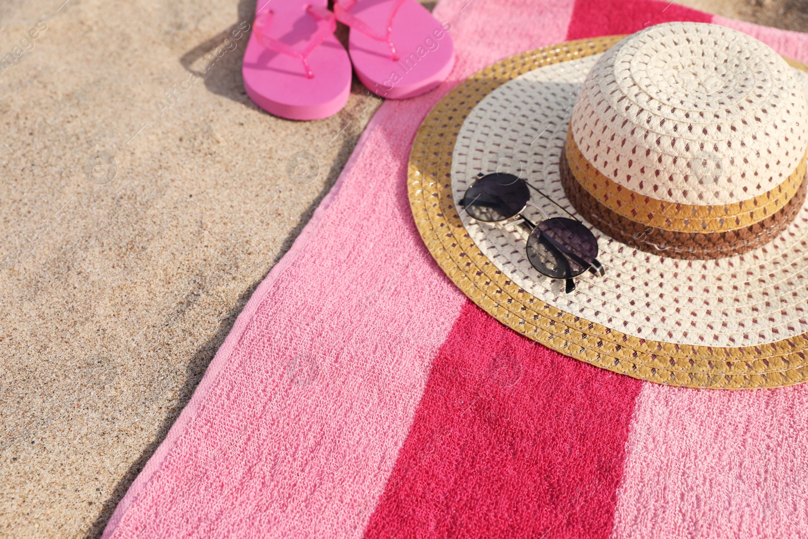 Photo of Beach towel with slippers, straw hat and sunglasses on sand