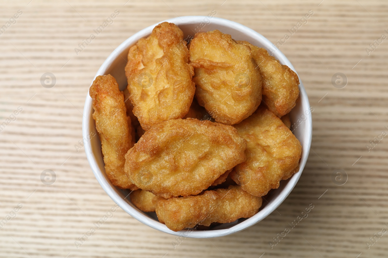 Photo of Bucket with tasty chicken nuggets on wooden table, top view