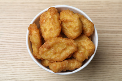 Photo of Bucket with tasty chicken nuggets on wooden table, top view