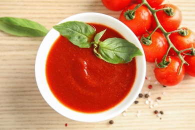 Bowl of tasty tomato sauce with basil on wooden table, flat lay