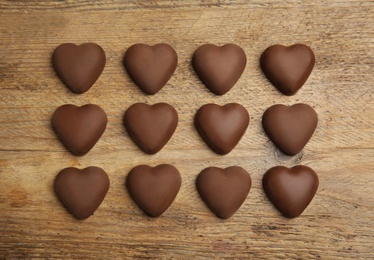 Photo of Tasty heart shaped chocolate candies on wooden table, flat lay. Happy Valentine's day