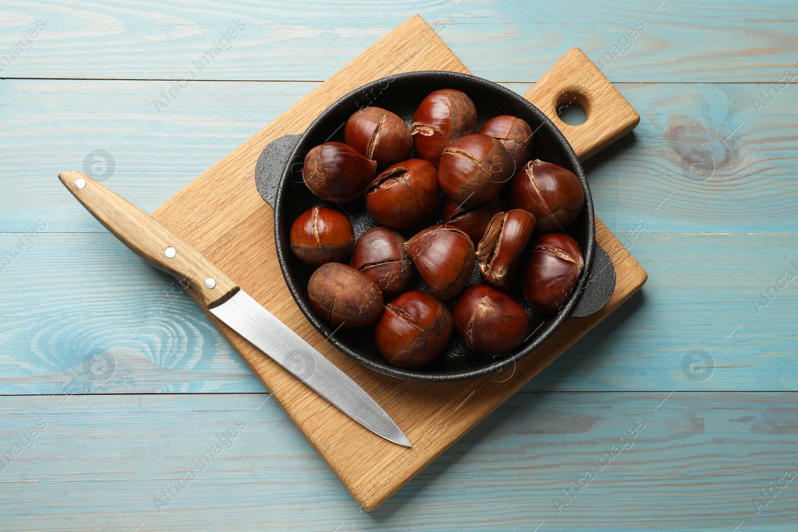 Photo of Fresh edible sweet chestnuts in frying pan on light blue wooden table, top view