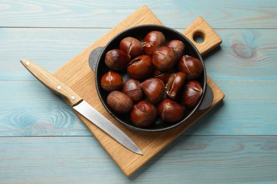 Photo of Fresh edible sweet chestnuts in frying pan on light blue wooden table, top view