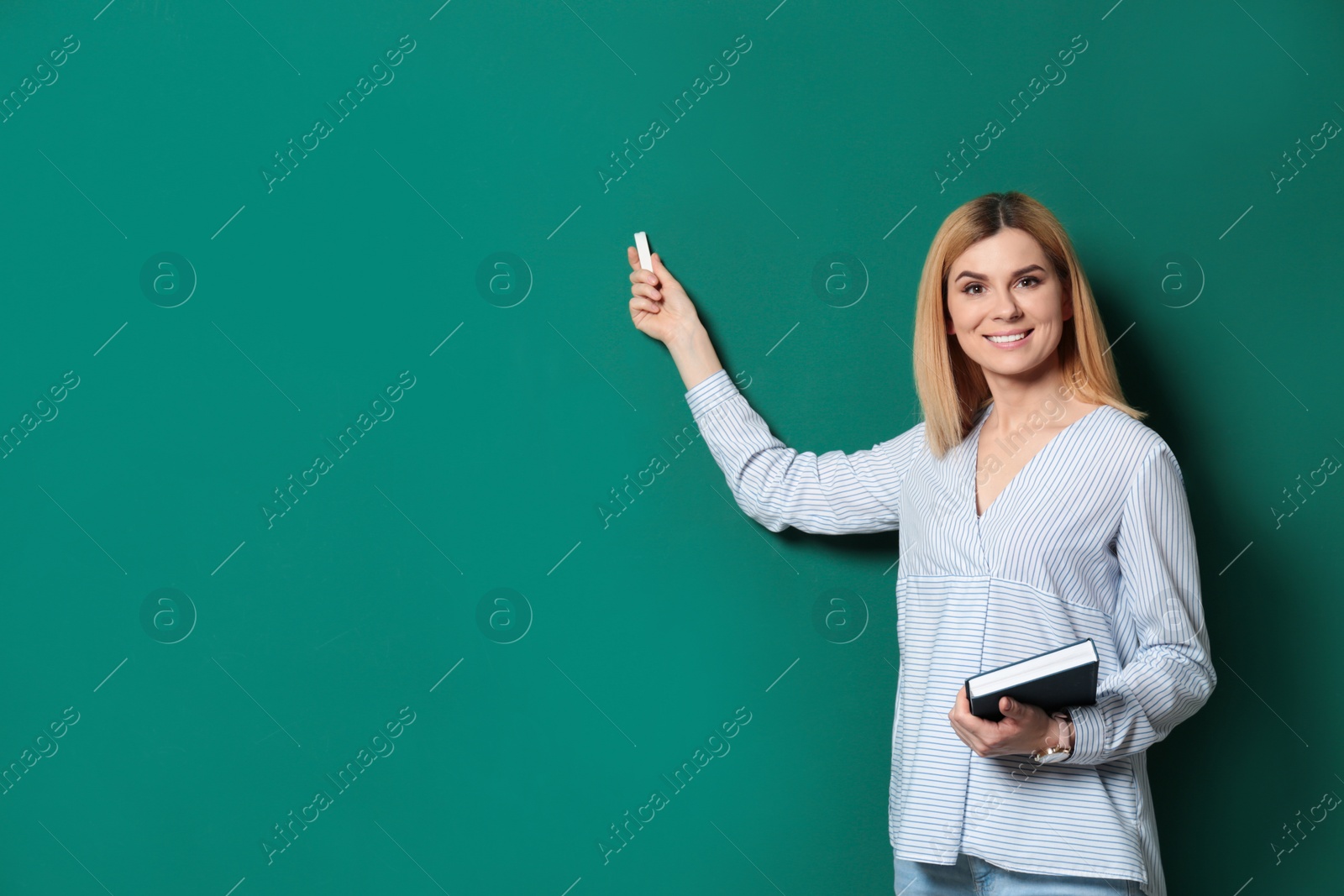 Photo of Beautiful teacher with book pointing at chalkboard, space for text
