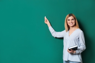 Beautiful teacher with book pointing at chalkboard, space for text