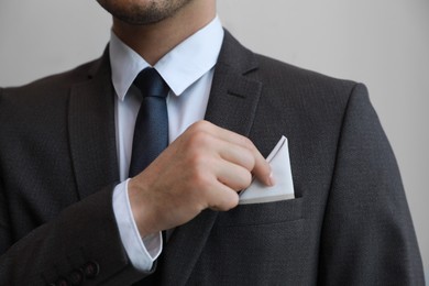 Man putting handkerchief into suit pocket on grey background, closeup