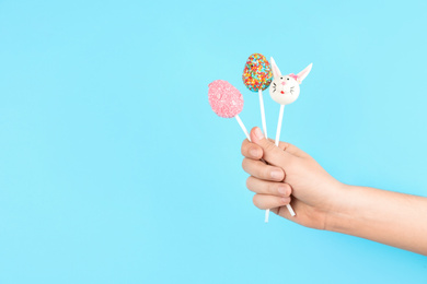 Photo of Closeup view of woman with delicious cake pops on light blue background, space for text. Easter holiday