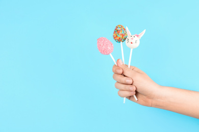 Closeup view of woman with delicious cake pops on light blue background, space for text. Easter holiday