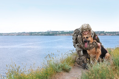 Man in military uniform with German shepherd dog near river